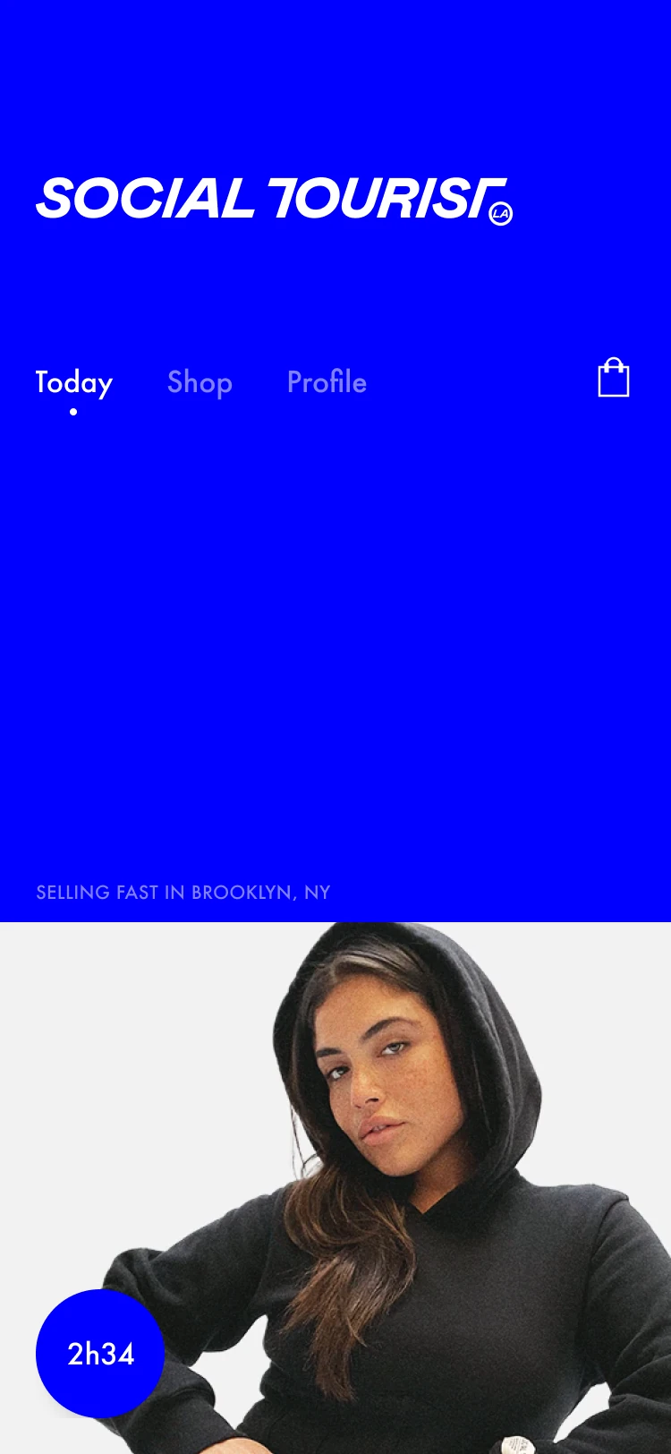 Social Tourist home screen with an electric-blue background, italic wordmark, shared navigation and a product-drop countdown.